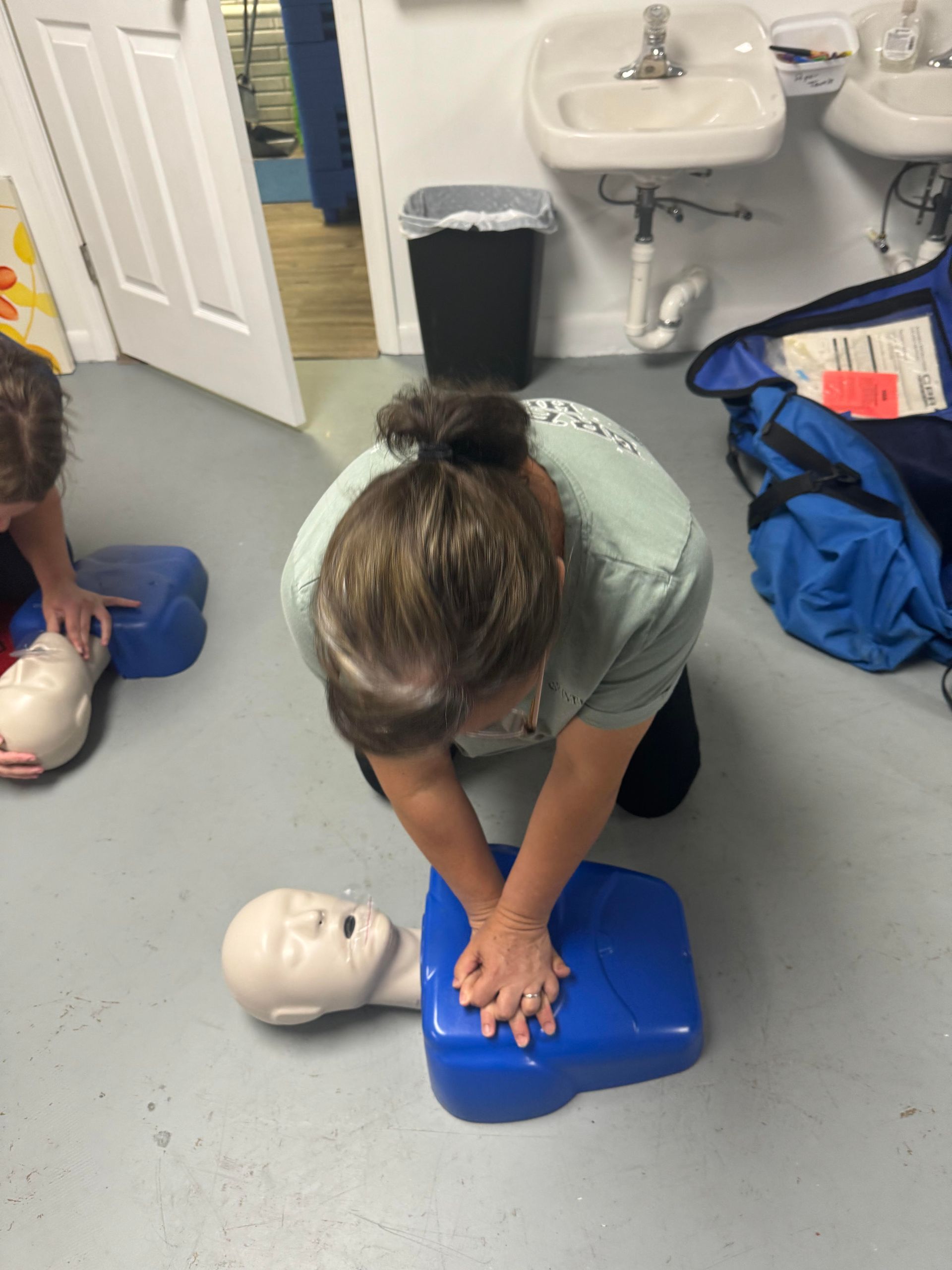 Person practicing CPR on a training dummy, indoors.