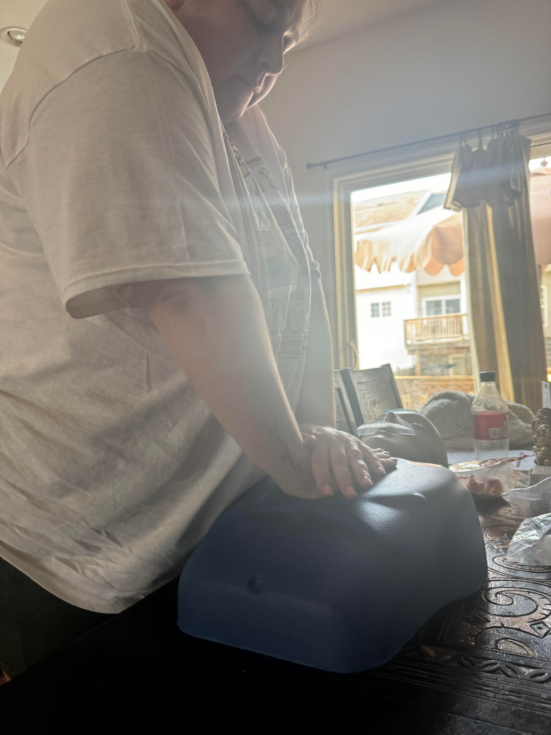 Person pressing down on a dark blue cushion on a table near a window.
