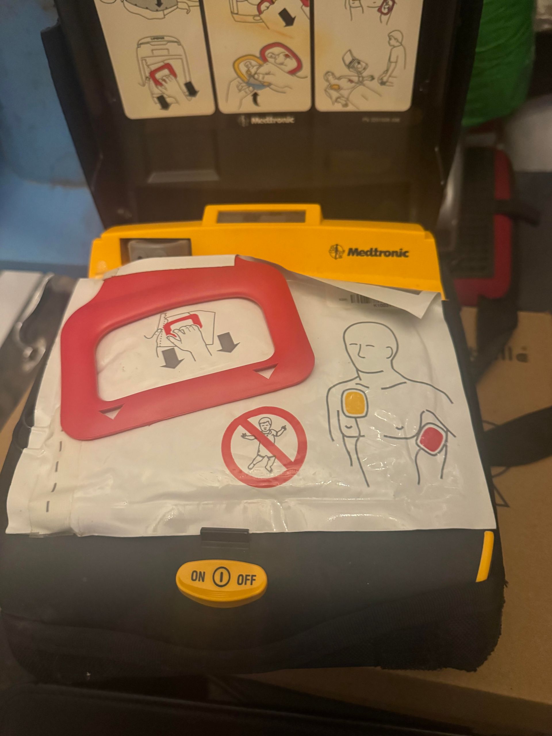Open AED case with yellow and black exterior, showing electrode pads and instructions.