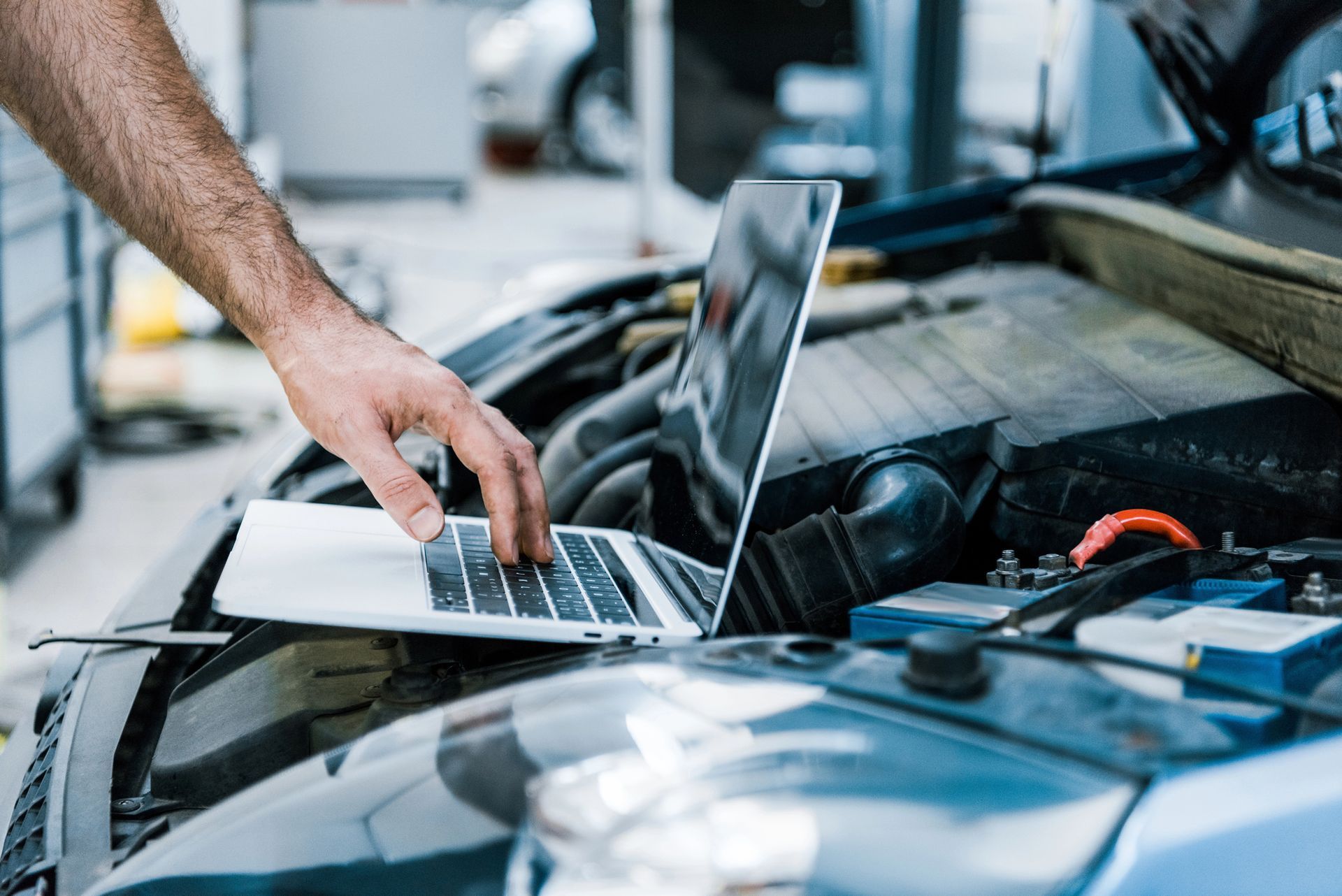 Un'auto nera con il cofano aperto, una batteria e un blocco sul motore in un'officina.