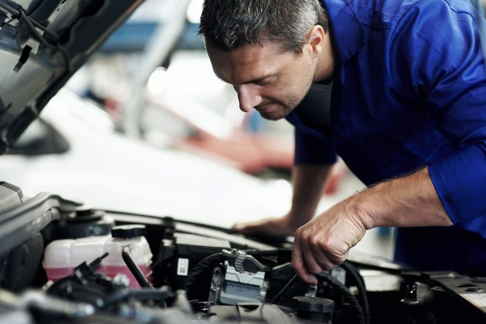 Un meccanico in camicia blu ispeziona il motore di un'auto in un'officina.