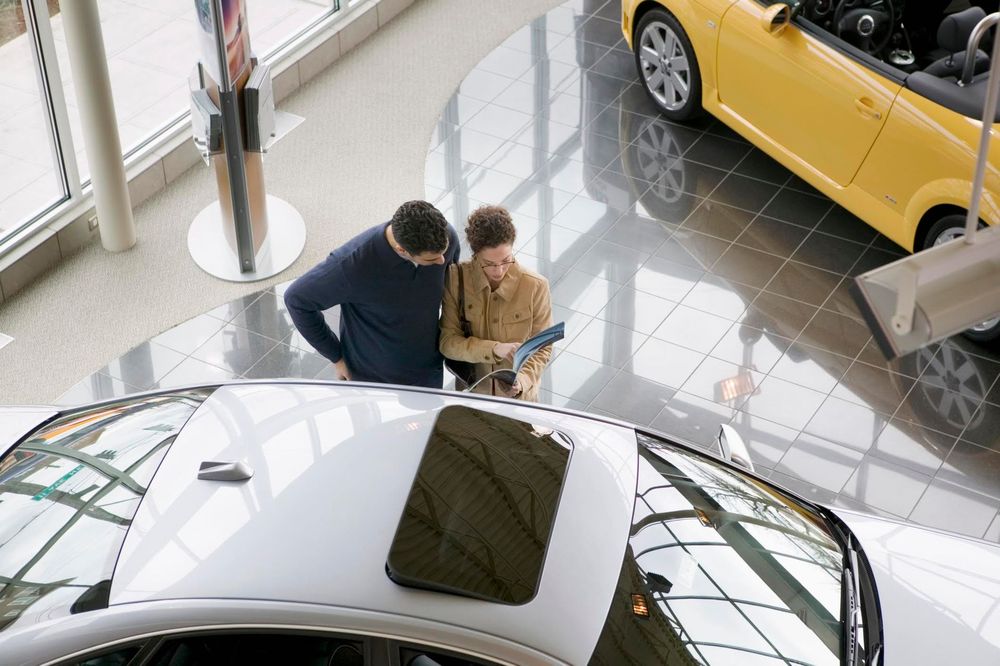 Due persone che sfogliano una brochure accanto a un'auto bianca in uno showroom luminoso.