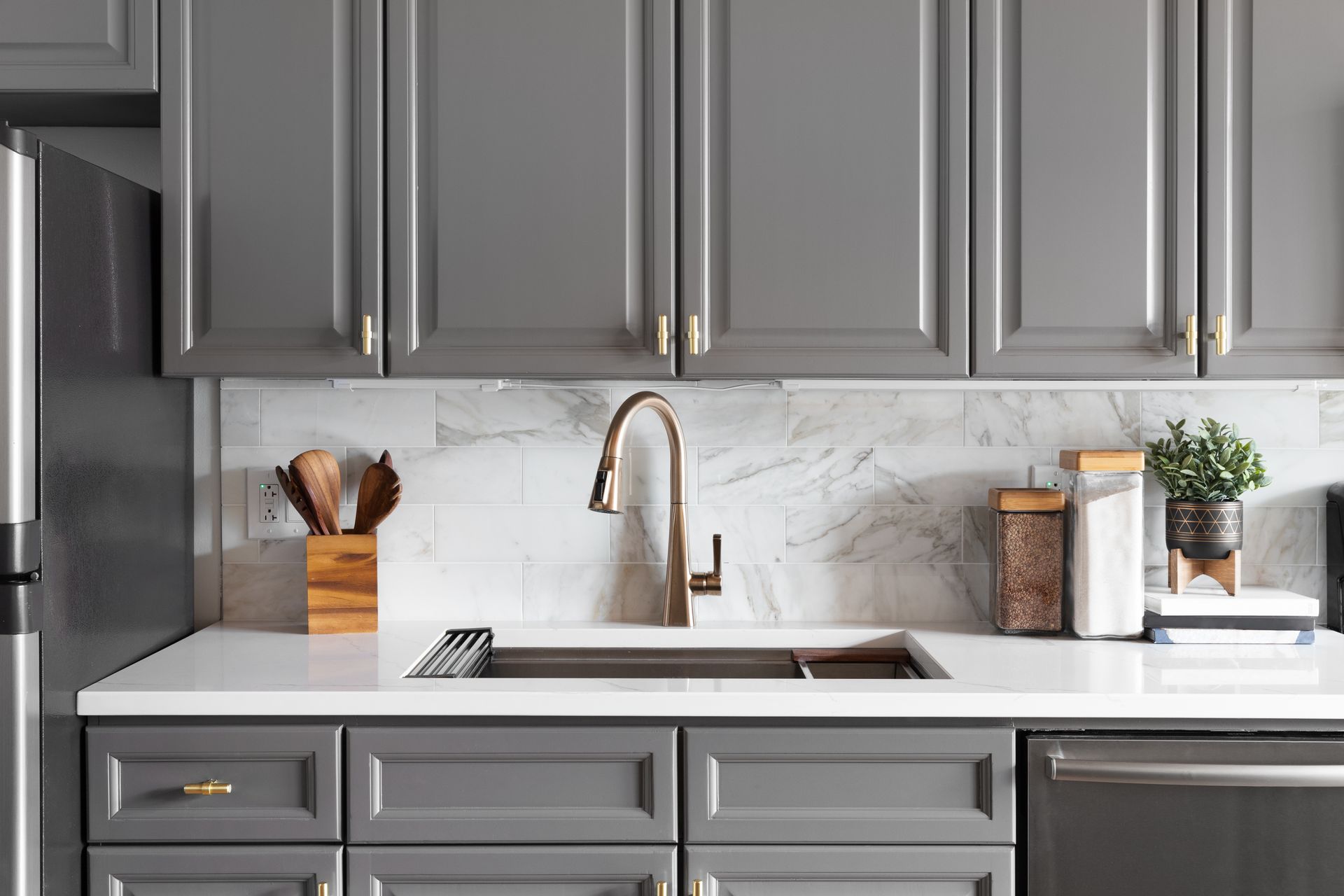 Gray kitchen cabinets with a white countertop and a bronze faucet.