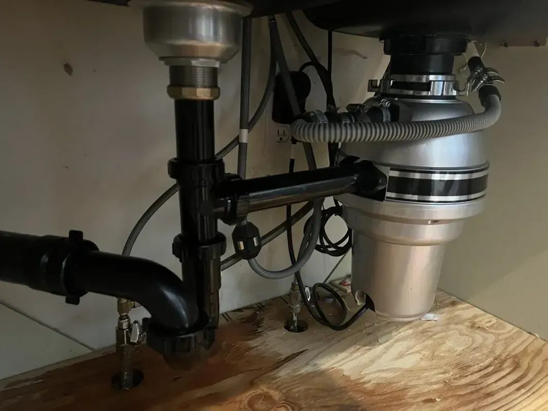 Under-sink plumbing with a garbage disposal and drain pipes in a kitchen.
