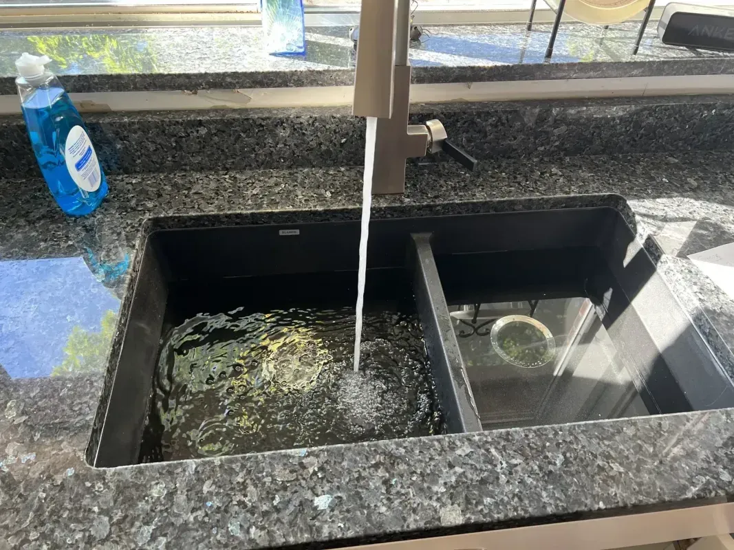 Sink with running water in a black granite countertop. Dish soap bottle on the left.
