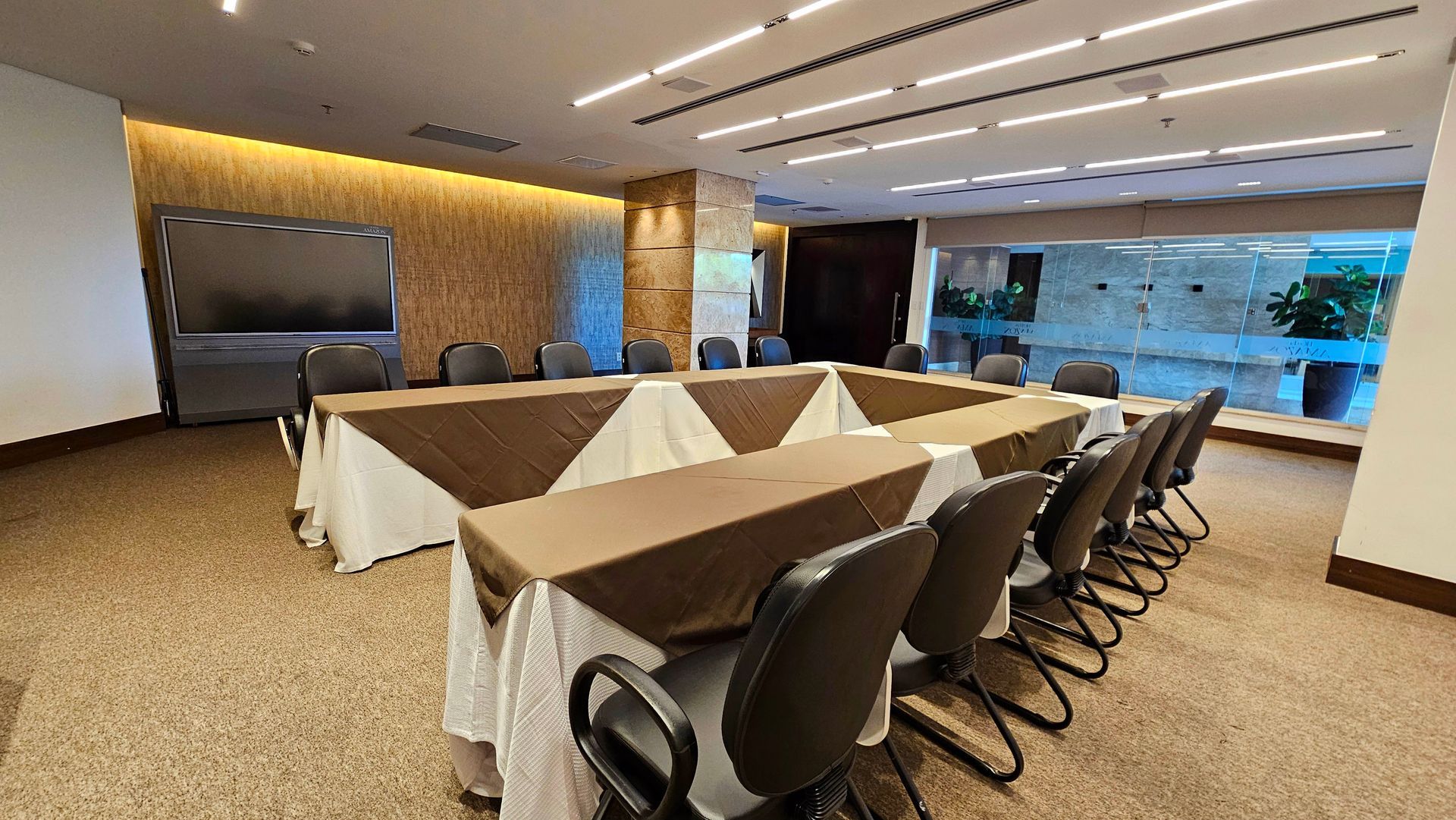 Sala de reuniões com mesa quadrada preparada para conferências; cadeiras ao redor da mesa, piso acarpetado.
