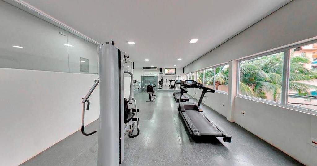 Academia com equipamentos de ginástica, janelas e iluminação abundante.