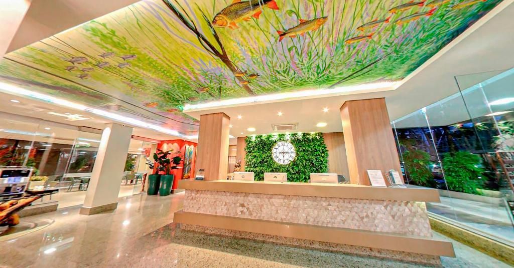 Hall de entrada do hotel com balcão de recepção e teto com mosaico representando a vida aquática.