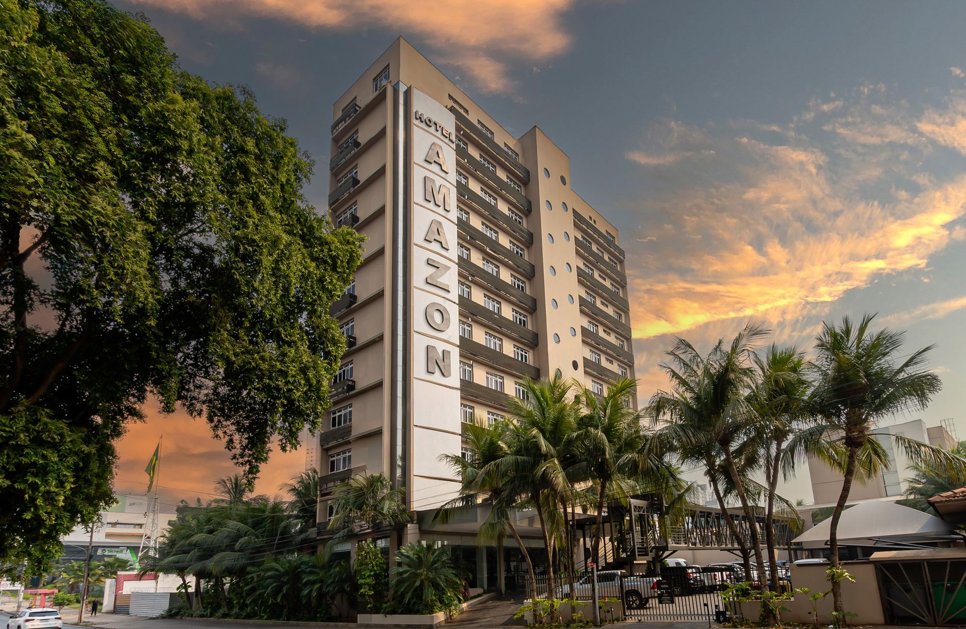 Edifício do Hotel Amazon com letras altas, palmeiras e céu ao pôr do sol.