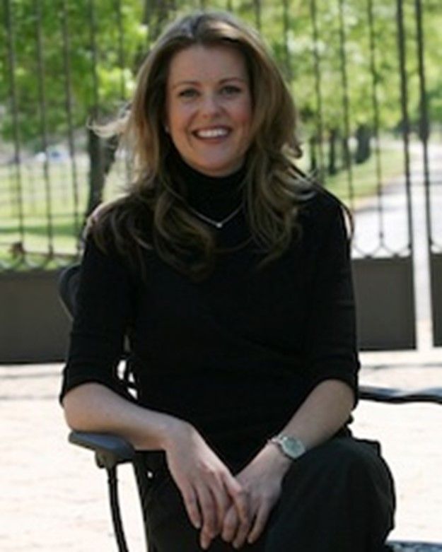 Woman smiling, sitting outdoors in black turtleneck, watch, near gate.