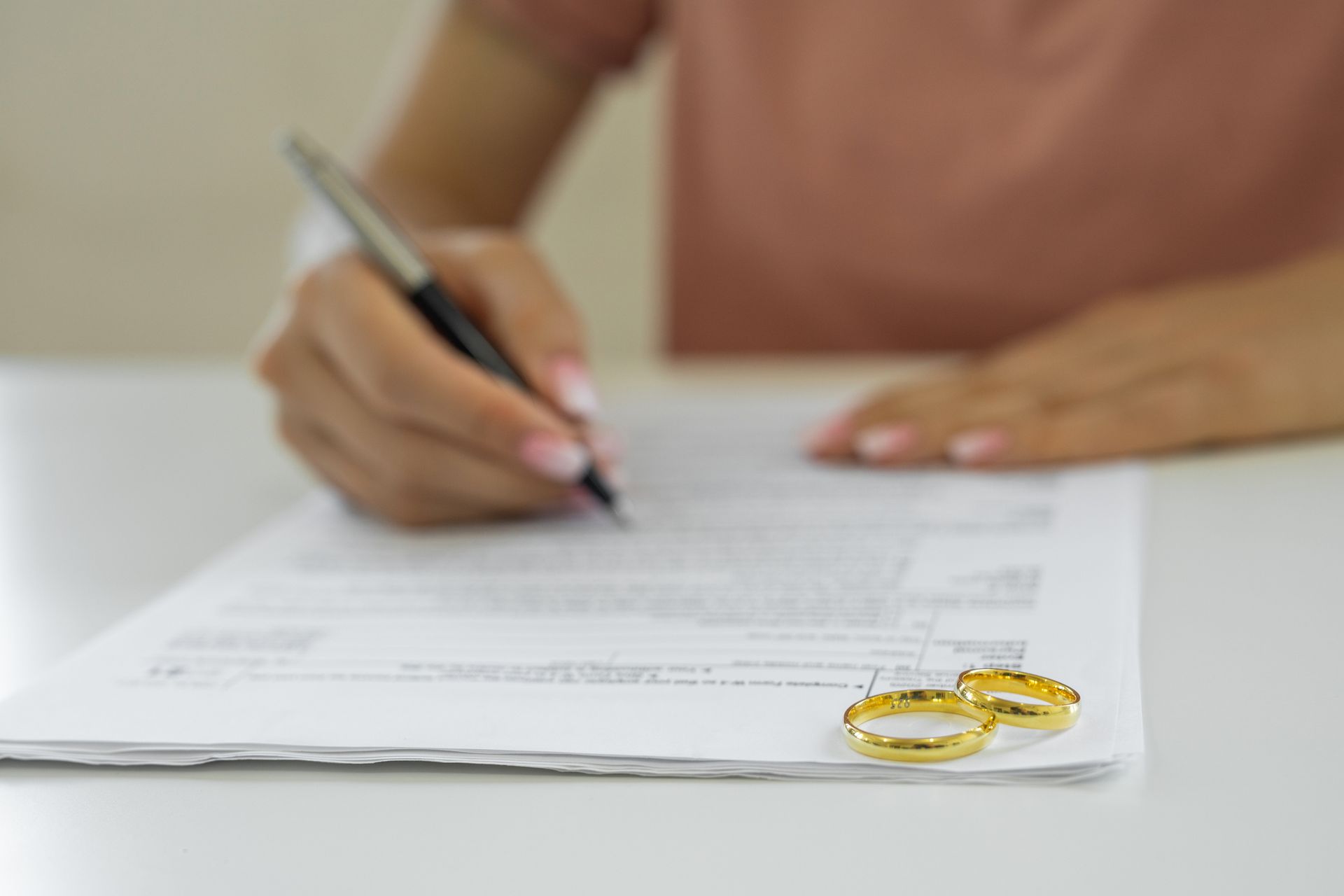 A person signs documents next to wedding rings, symbolizing help from a divorce lawyer.
