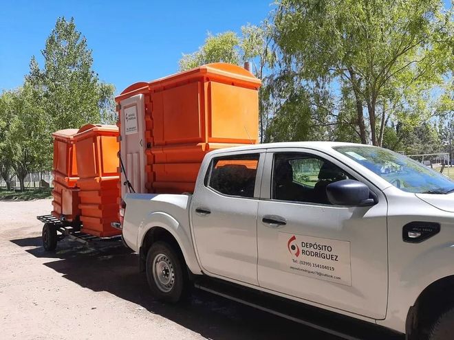 Camioneta blanca remolcando dos remolques naranjas en una carretera soleada bordeada de árboles.