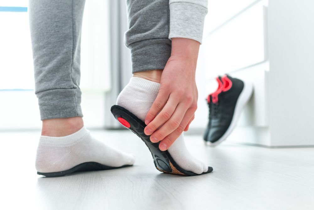 Person Inserts an Insole Into a Shoe While Wearing a Sock, Indoors — Biomedical Sports Podiatry in Forster, NSW