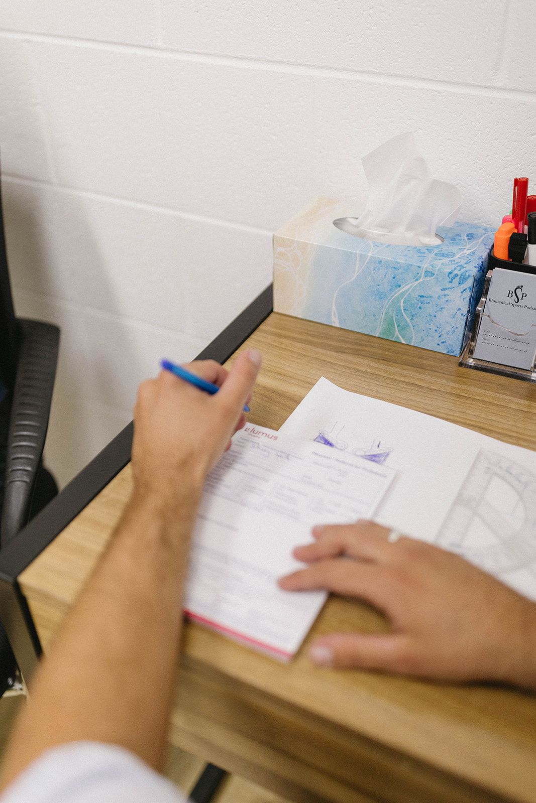 Person Writing on a Document at a Desk With Tissues and Pens Nearby — Biomedical Sports Podiatry in Forster, NSW