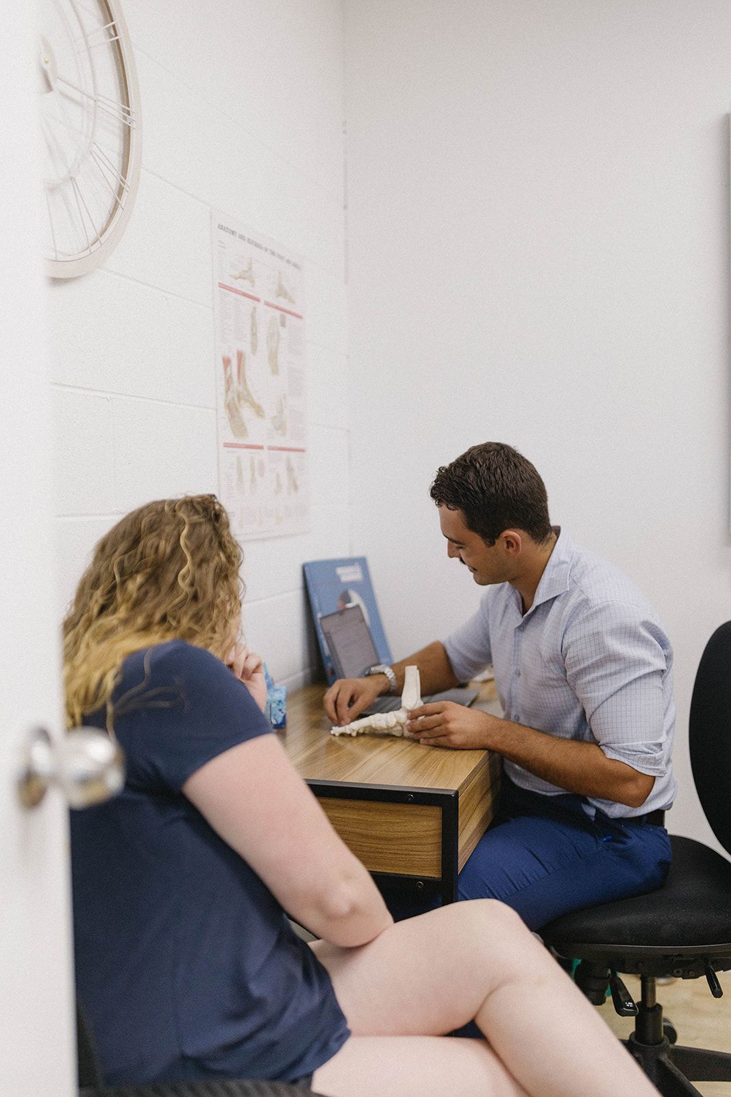 Two people sitting at a small table, working together on a laptop in a white office room — Biomedical Sports Podiatry in Forster, NSW