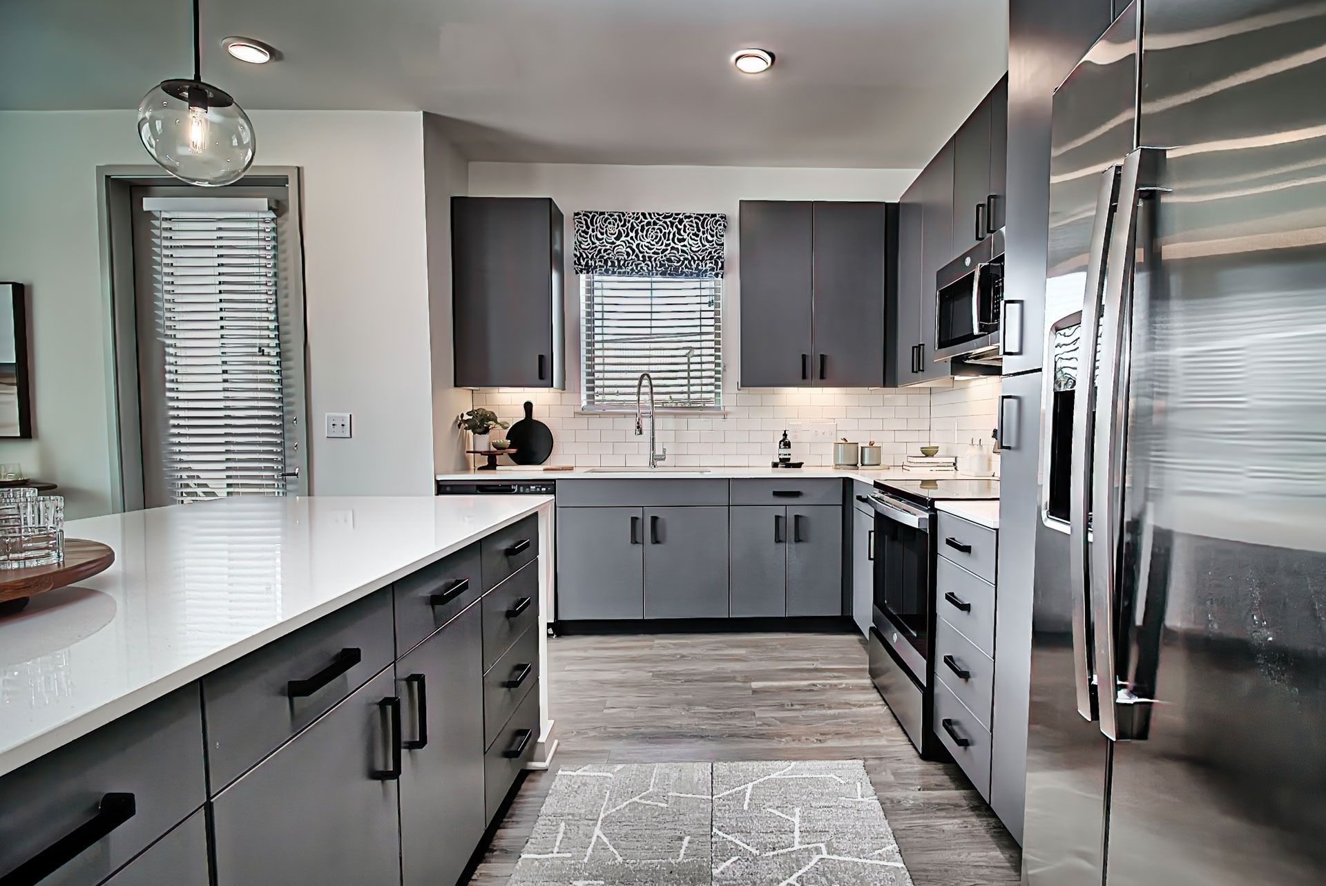 Modern kitchen with gray cabinets, white countertops, stainless steel appliances, and a patterned rug.