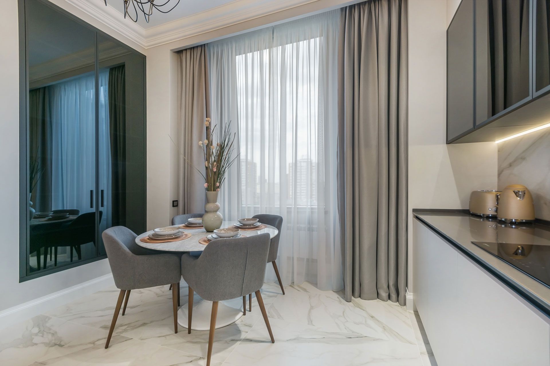 Dining area with round table, grey chairs, sheer curtains, dark cabinets, and marble flooring.