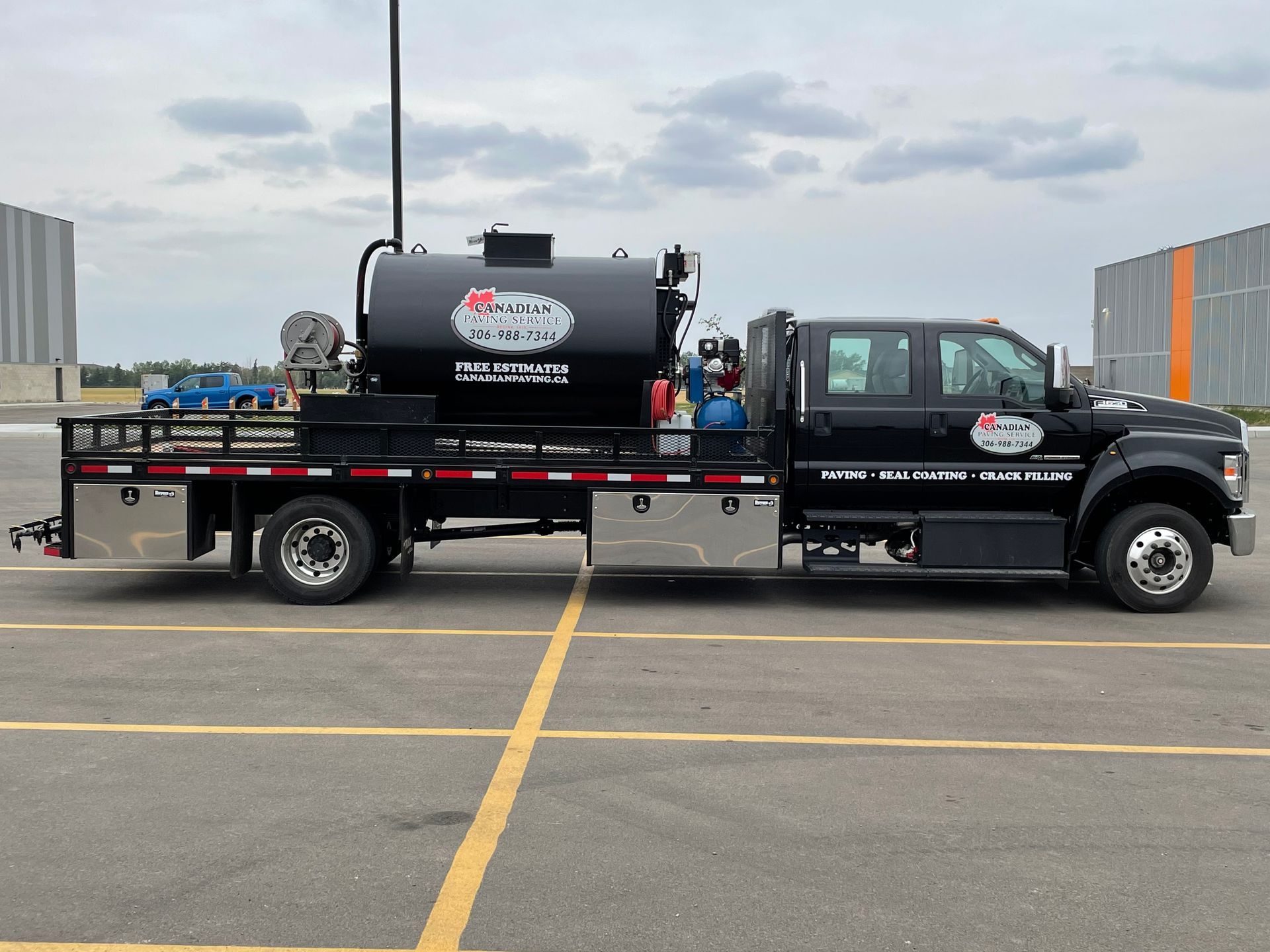 A black utility truck with a large fuel tank mounted on its flatbed parked in a paved lot.
