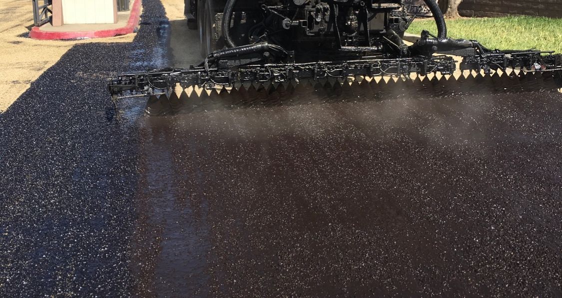 An asphalt distributor truck spraying hot liquid bitumen onto a road surface during a paving project.