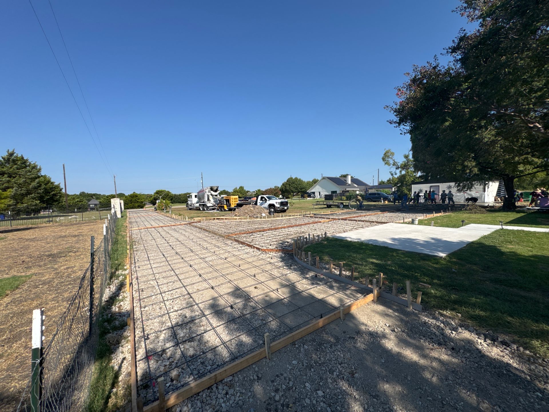 Construction site with a concrete driveway and foundation forms, under a blue sky.