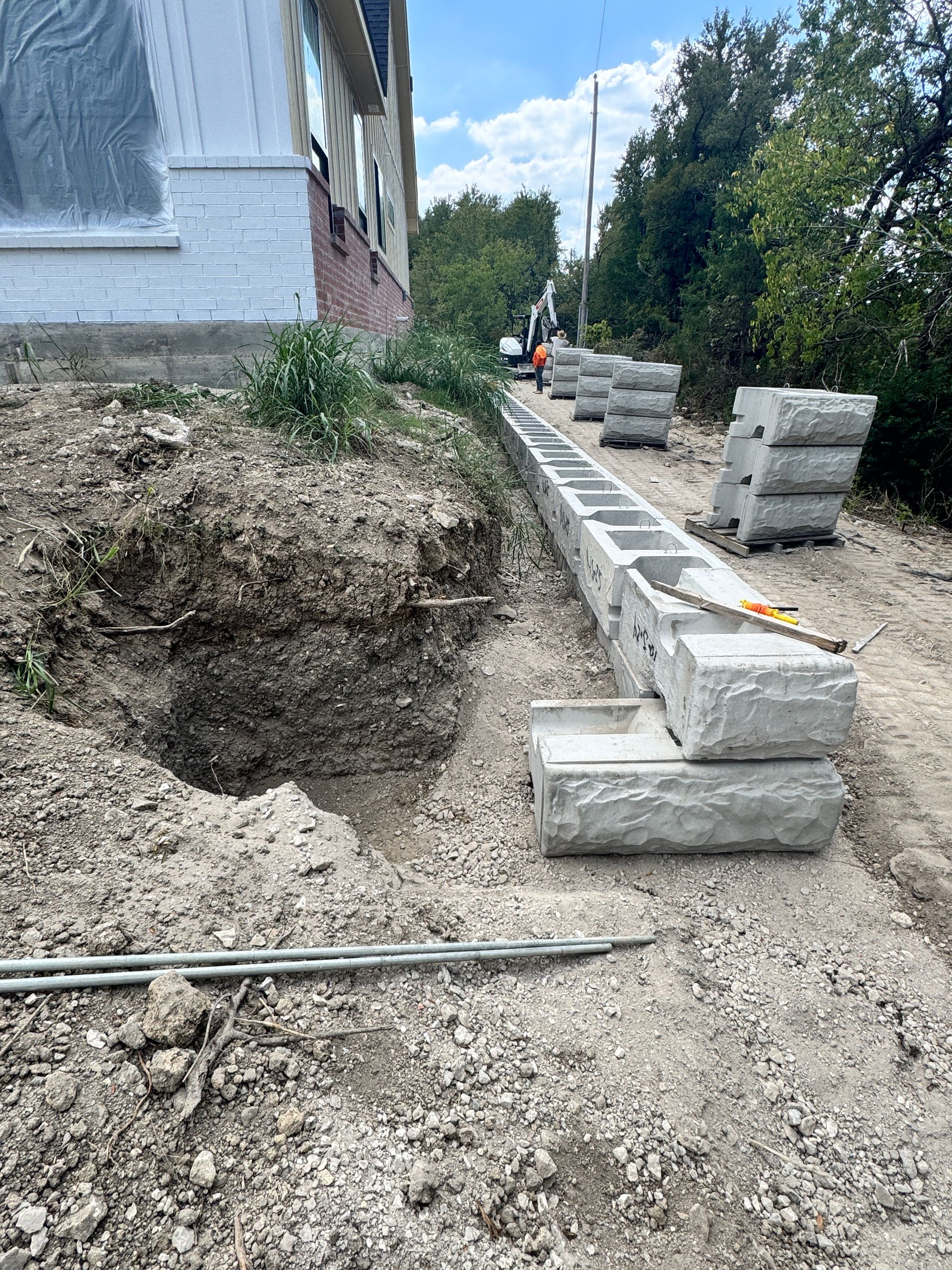 Construction site with a retaining wall being built. Stone blocks and digging on a hillside beside a building.