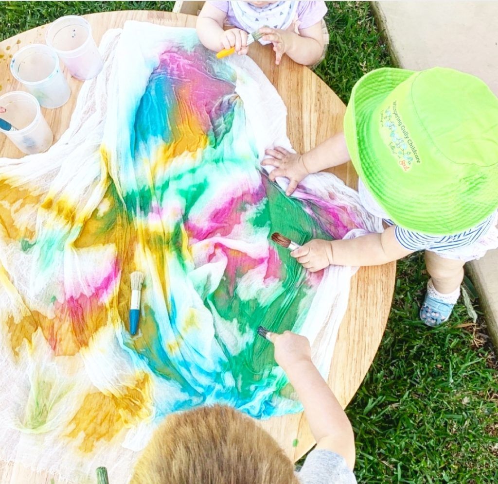 a group of children are sitting at a table playing with paint . Childcare Montessori Gold Coast Jindabyne