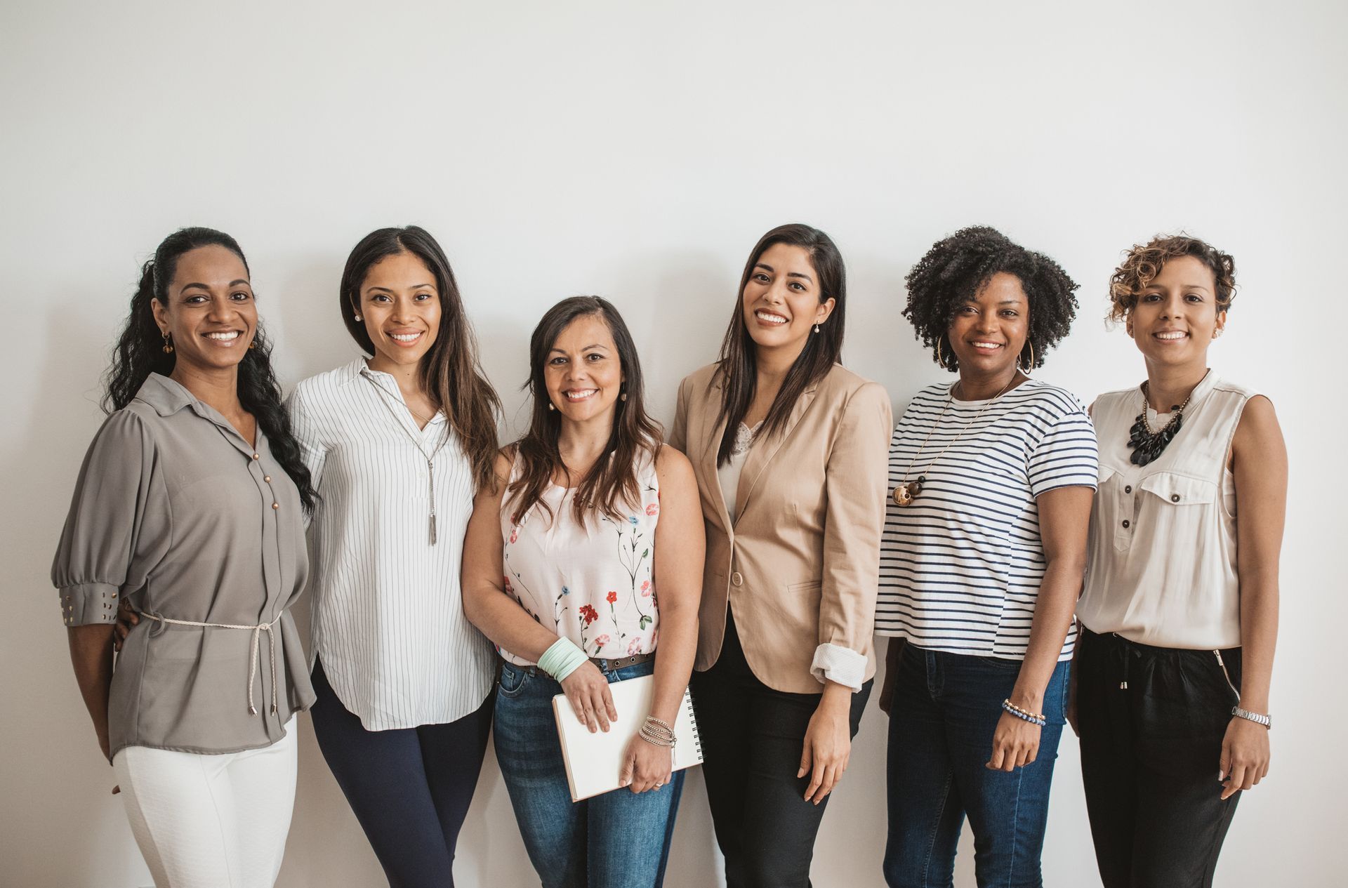 A group of women are standing next to each other in front of a white wall.