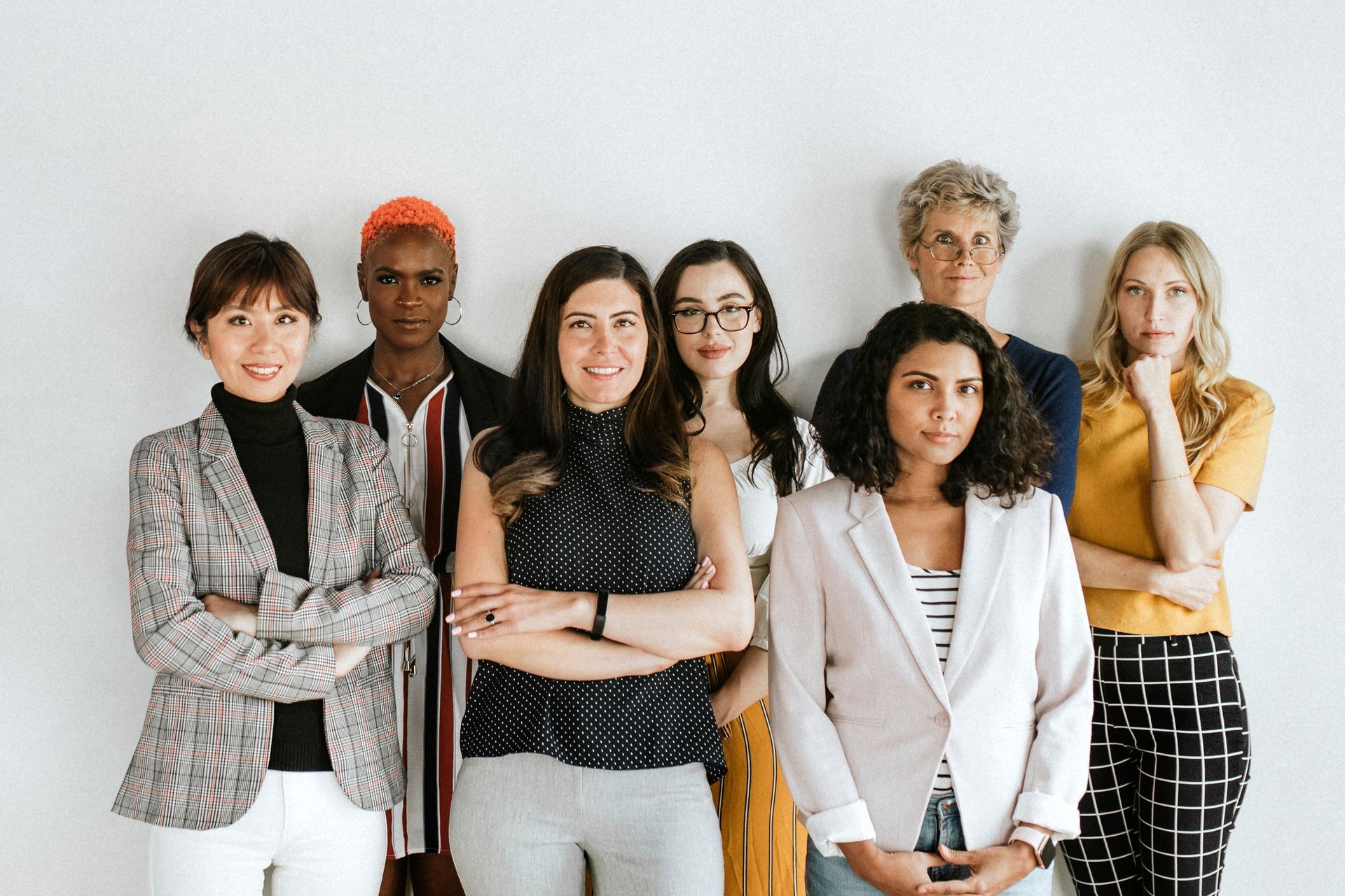 A group of women are standing next to each other in front of a white wall.