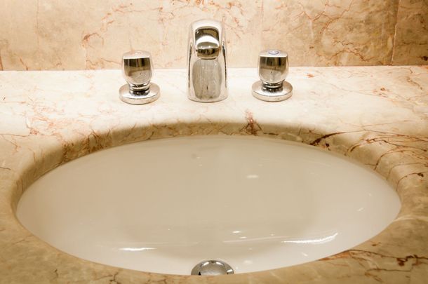 Marble bathroom sink with chrome faucet and beige countertop under warm lighting