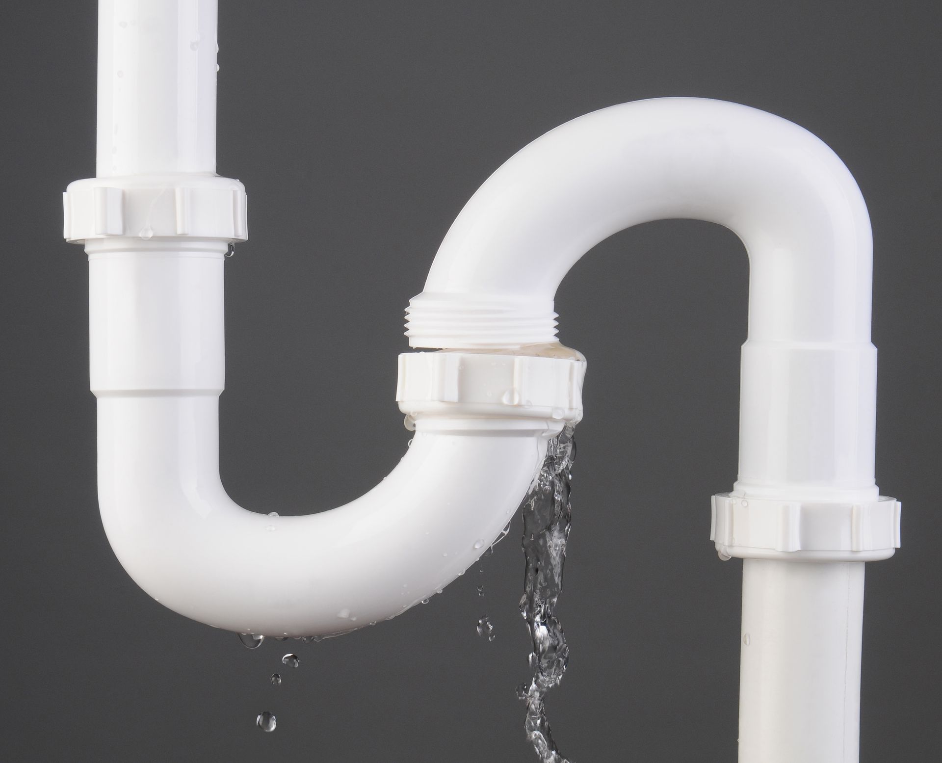 Leaking white PVC sink pipe with water dripping from a joint