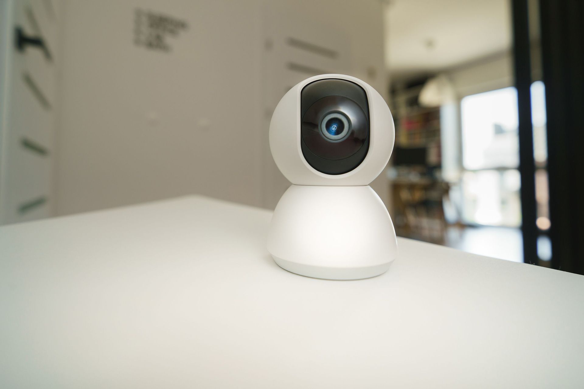White security camera with black lens on a table in a bright room.