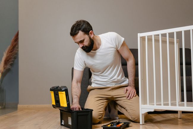 Man kneeling on the floor beside an open toolbox, working next to a white pet crate in a room