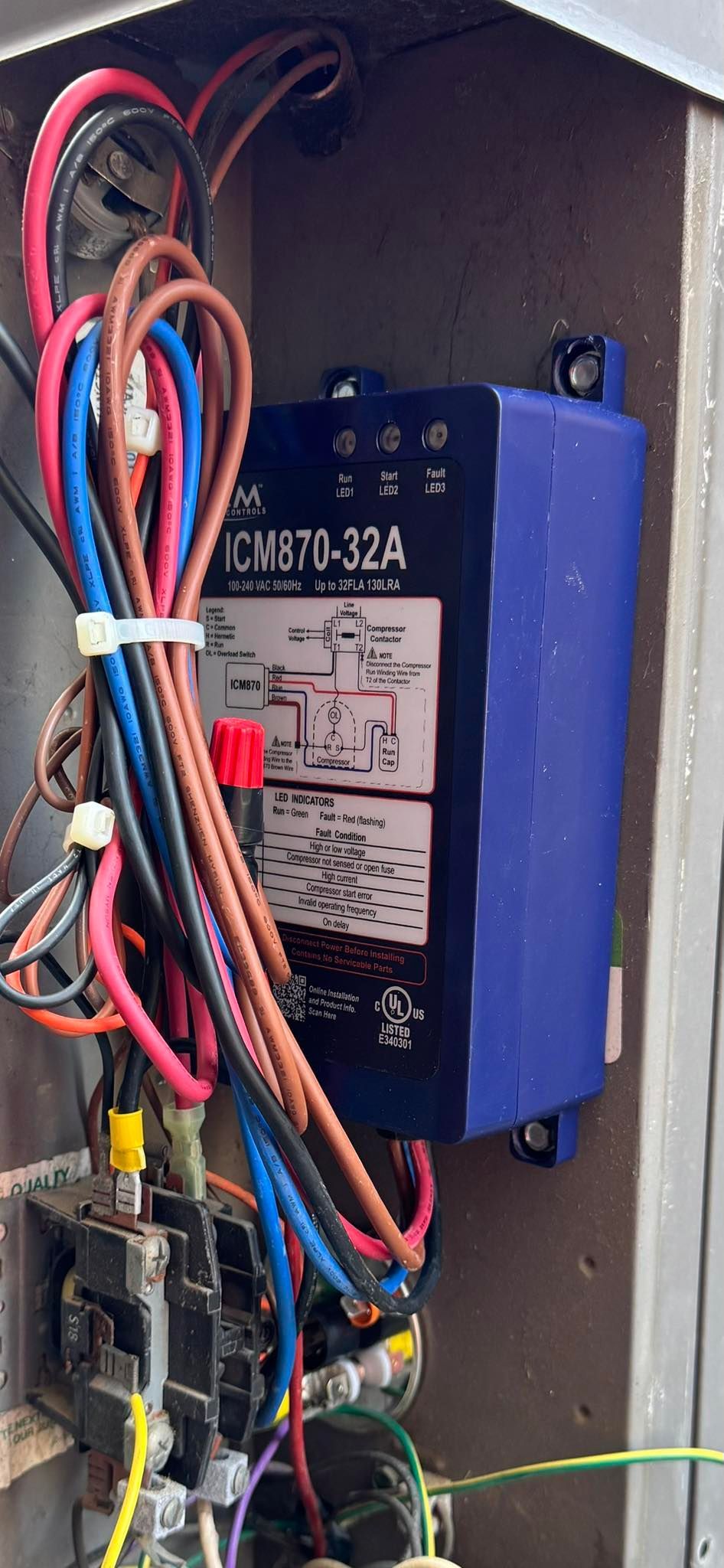 Open electrical panel with multicolored wires and a black-and-blue control module inside.