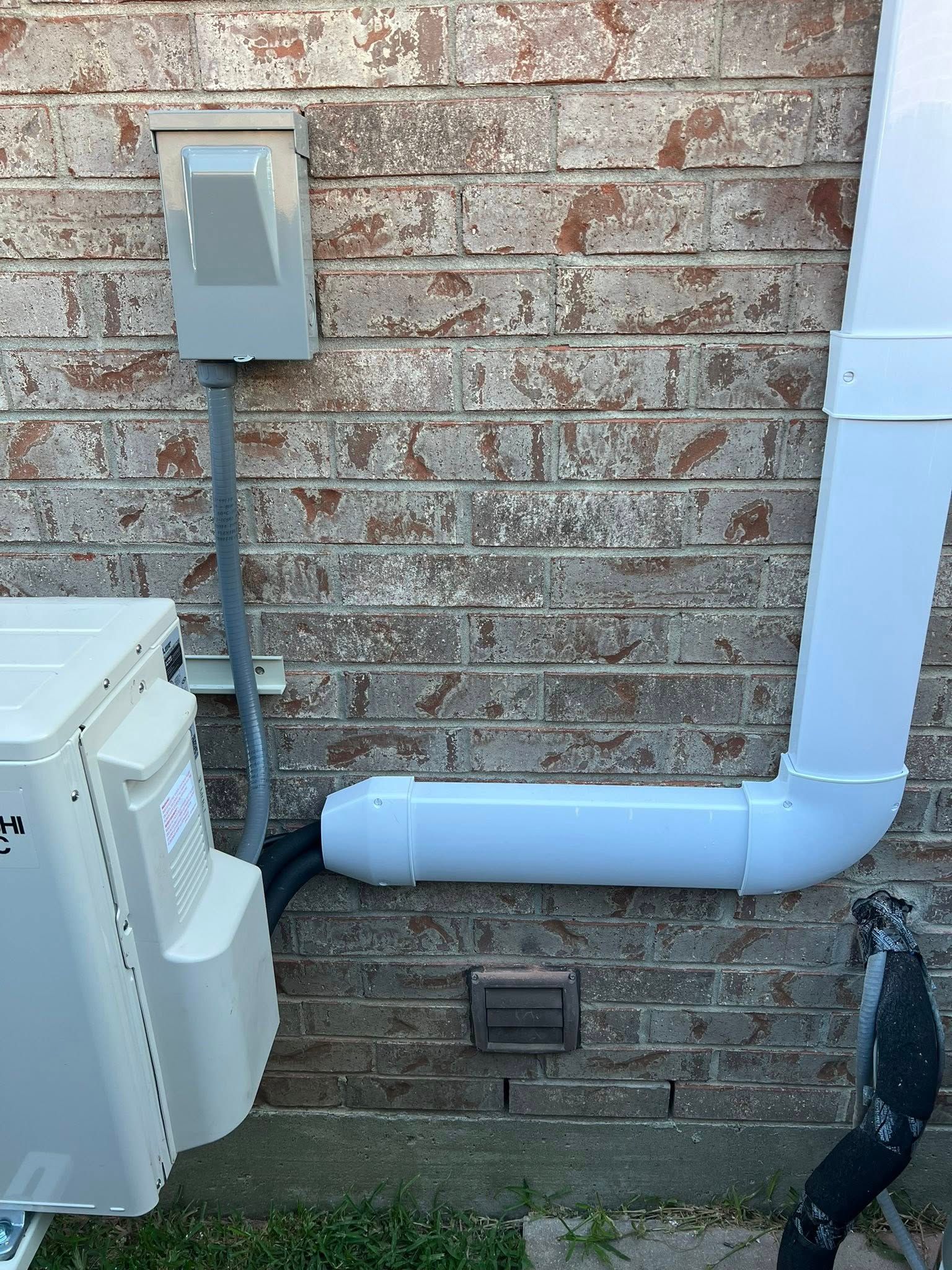 Brick exterior wall with gray utility box, white pipe, and HVAC equipment mounted near the ground.