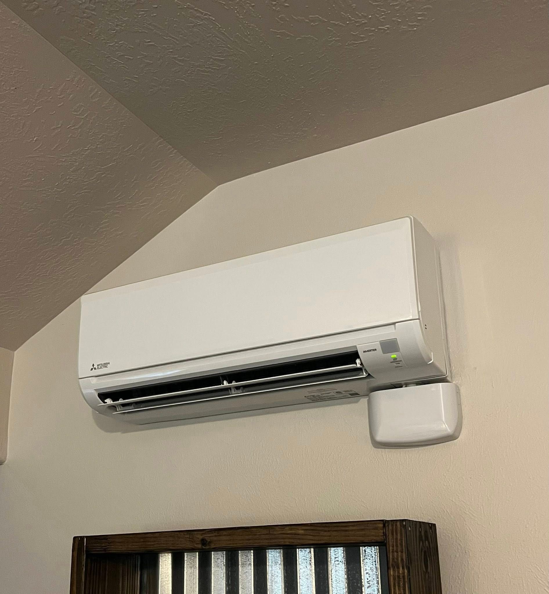 Wall-mounted white air conditioner above a wooden window frame in a corner room.