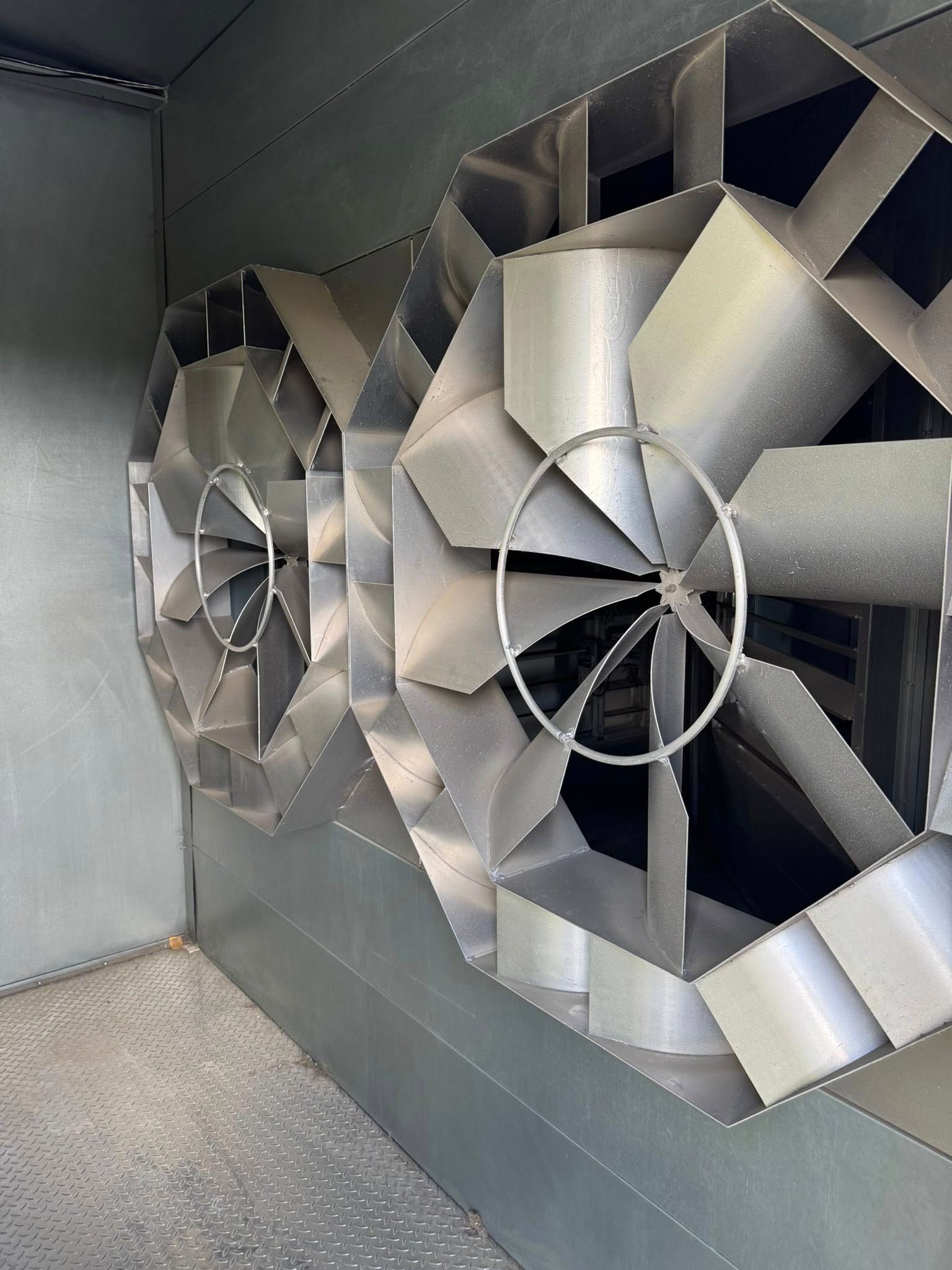 Two large silver industrial fans mounted in a metal enclosure with a textured floor