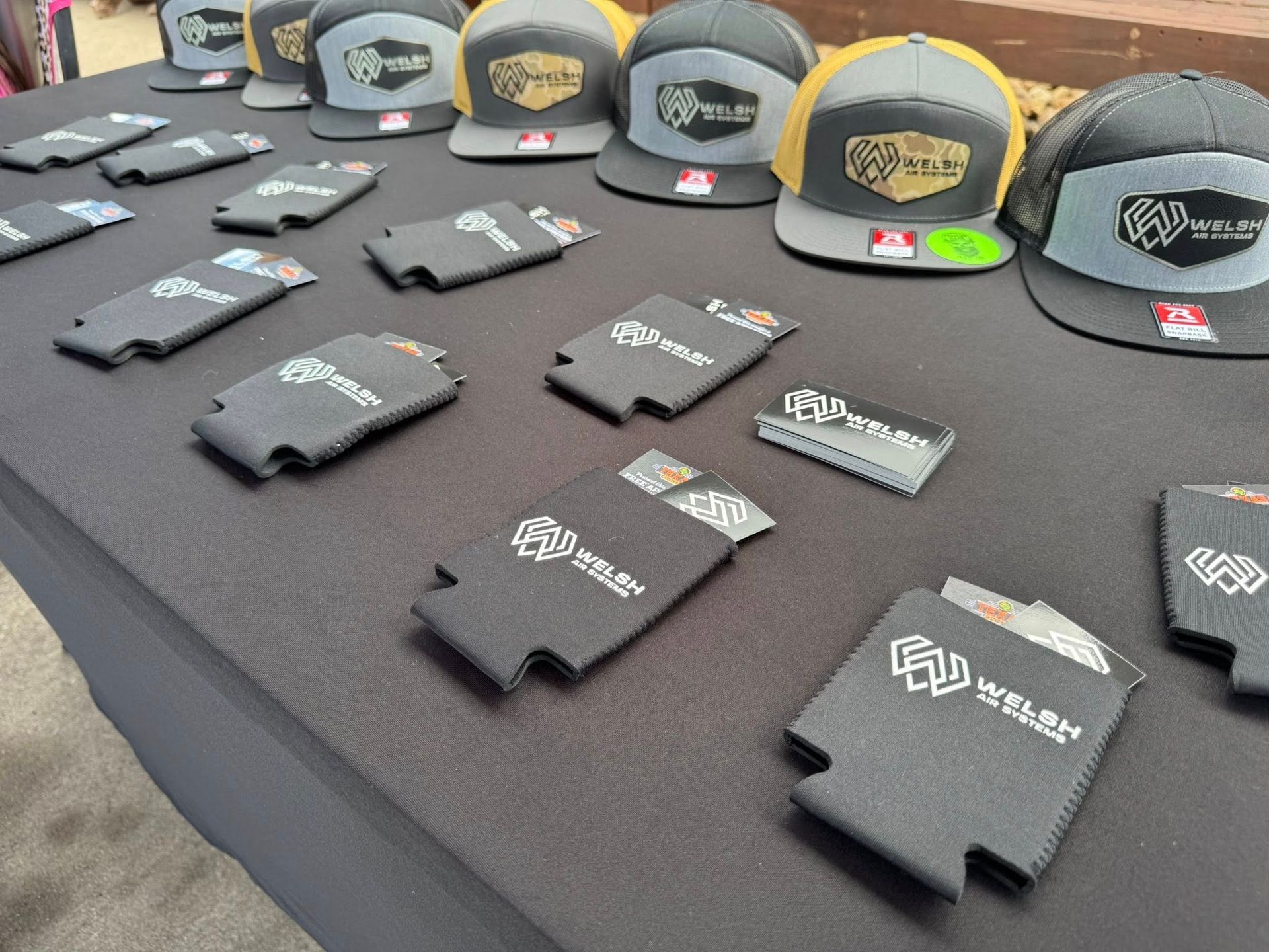 Table display of branded hats and folded shirts with logos on a black cloth backdrop.