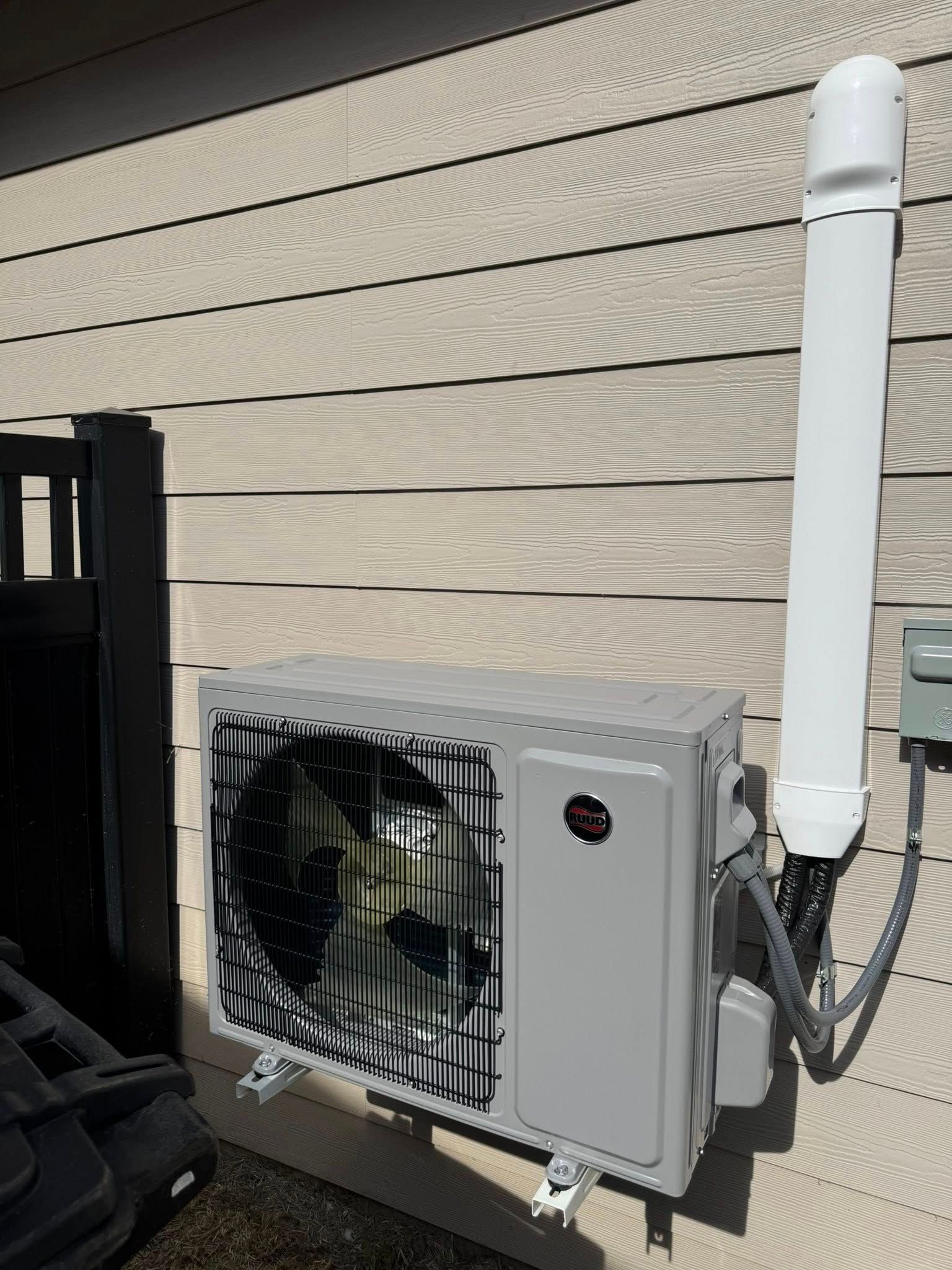 Outdoor HVAC unit mounted on a beige house wall next to a white vertical pipe.