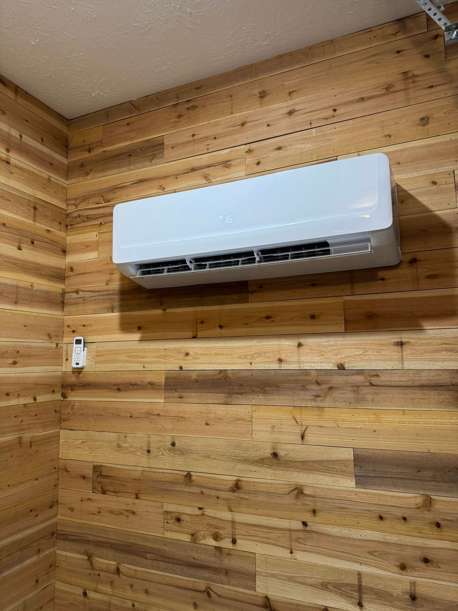 White wall-mounted air conditioner on a wood-paneled wall in a room corner