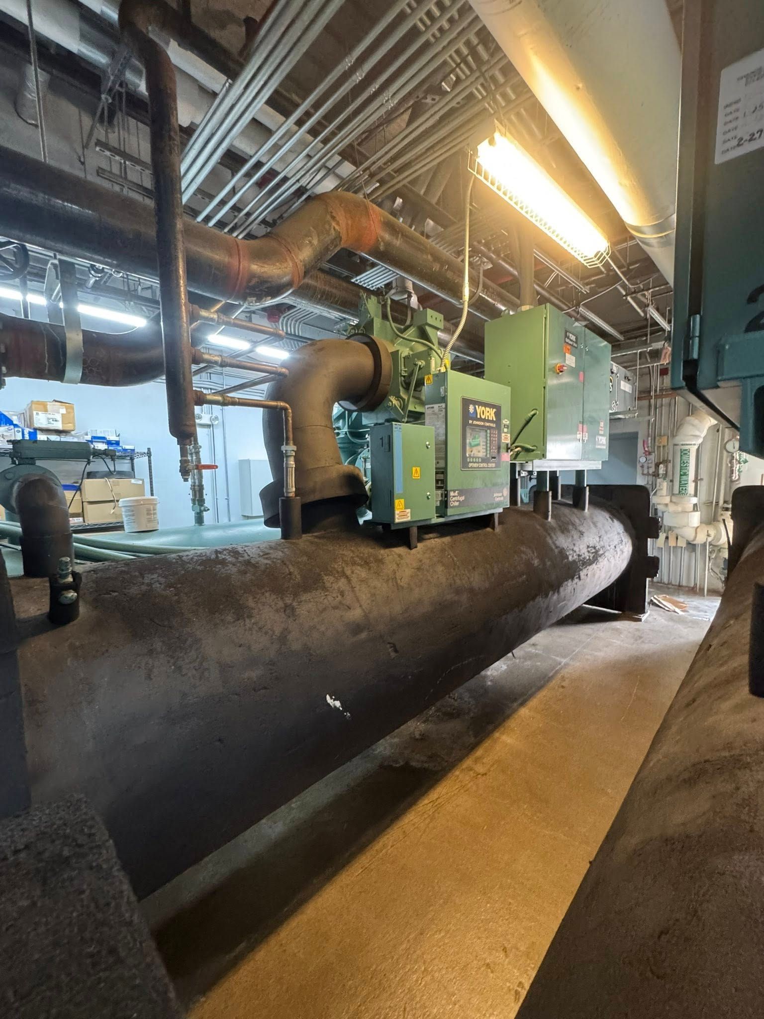Worker operating green industrial machine in a factory beside a large black pipe