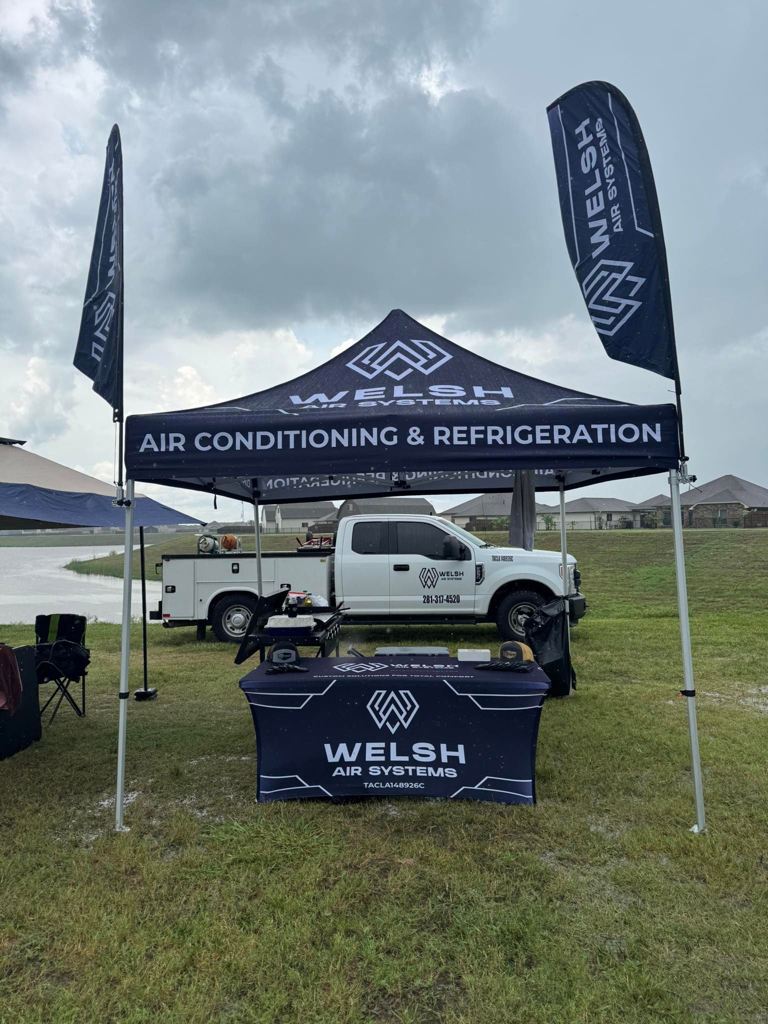 Welsh Air Conditioning & Refrigeration tent display with white pickup truck on grass under cloudy sky