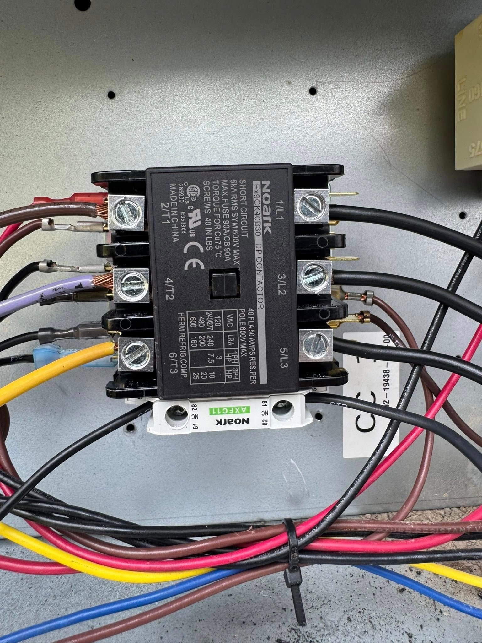 Electrical control module with multiple colored wires mounted inside a metal panel.