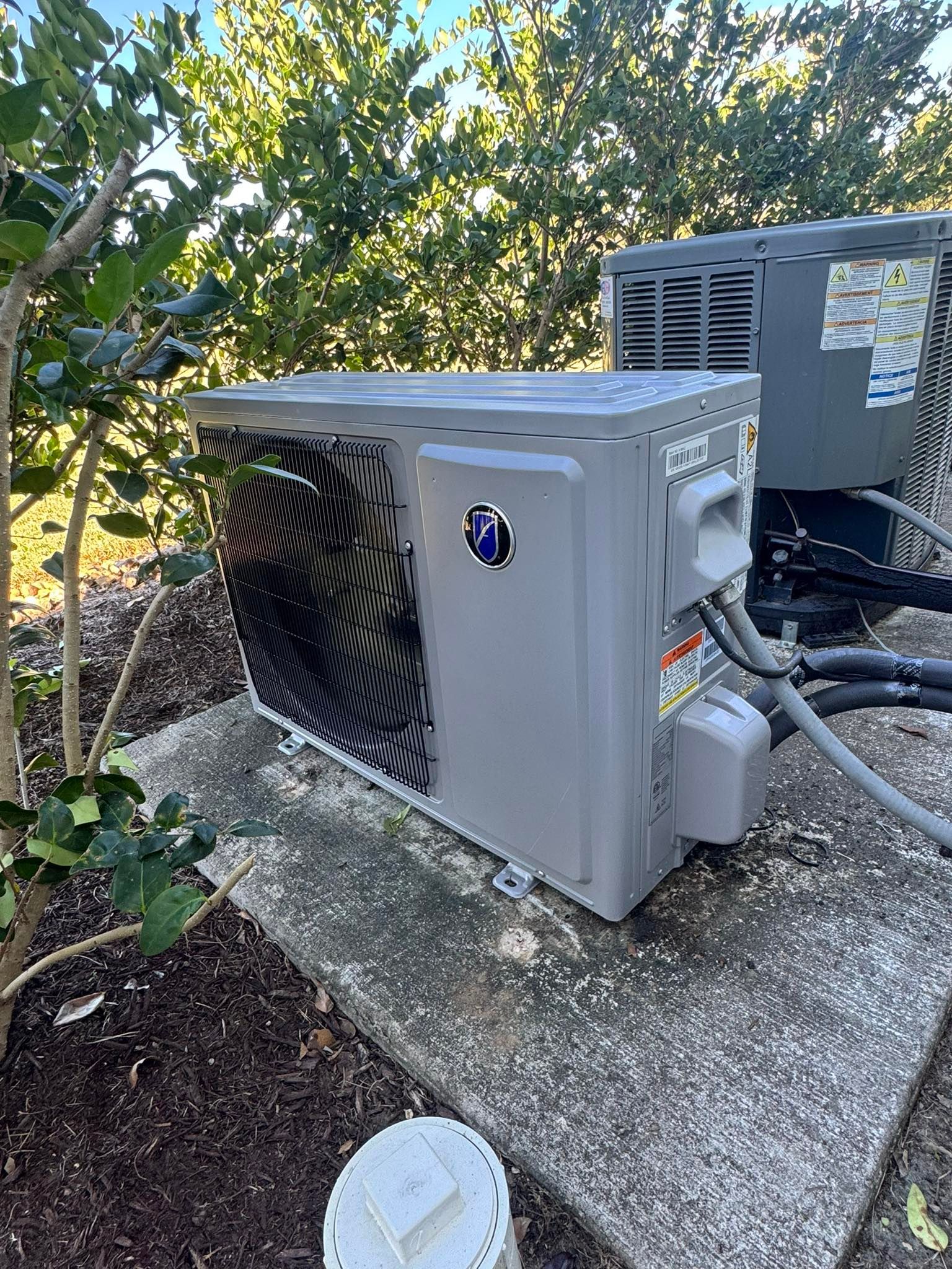 Outdoor HVAC condenser unit on a concrete pad beside a building, with trees in the background.