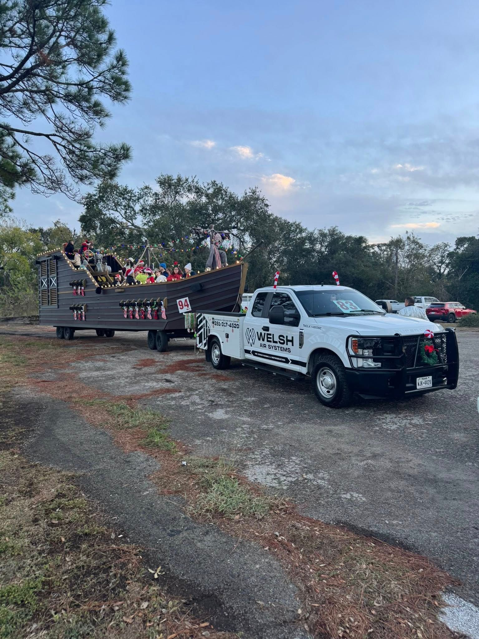Pickup truck towing a trailer of people along a gravel road at dusk, with trees and open sky nearby