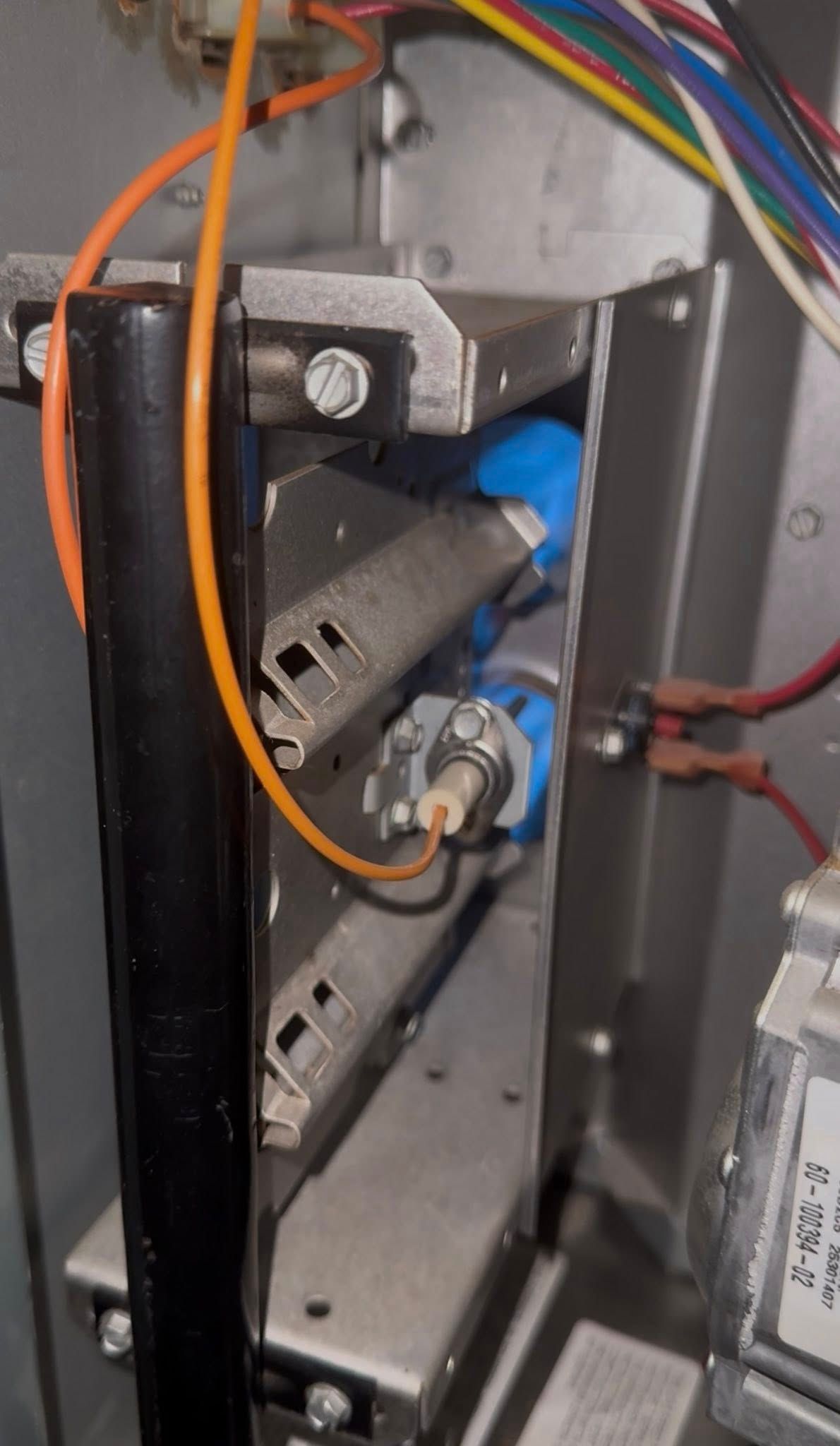 Close-up of wiring and metal components inside an electrical panel, with orange cables and a blue connector