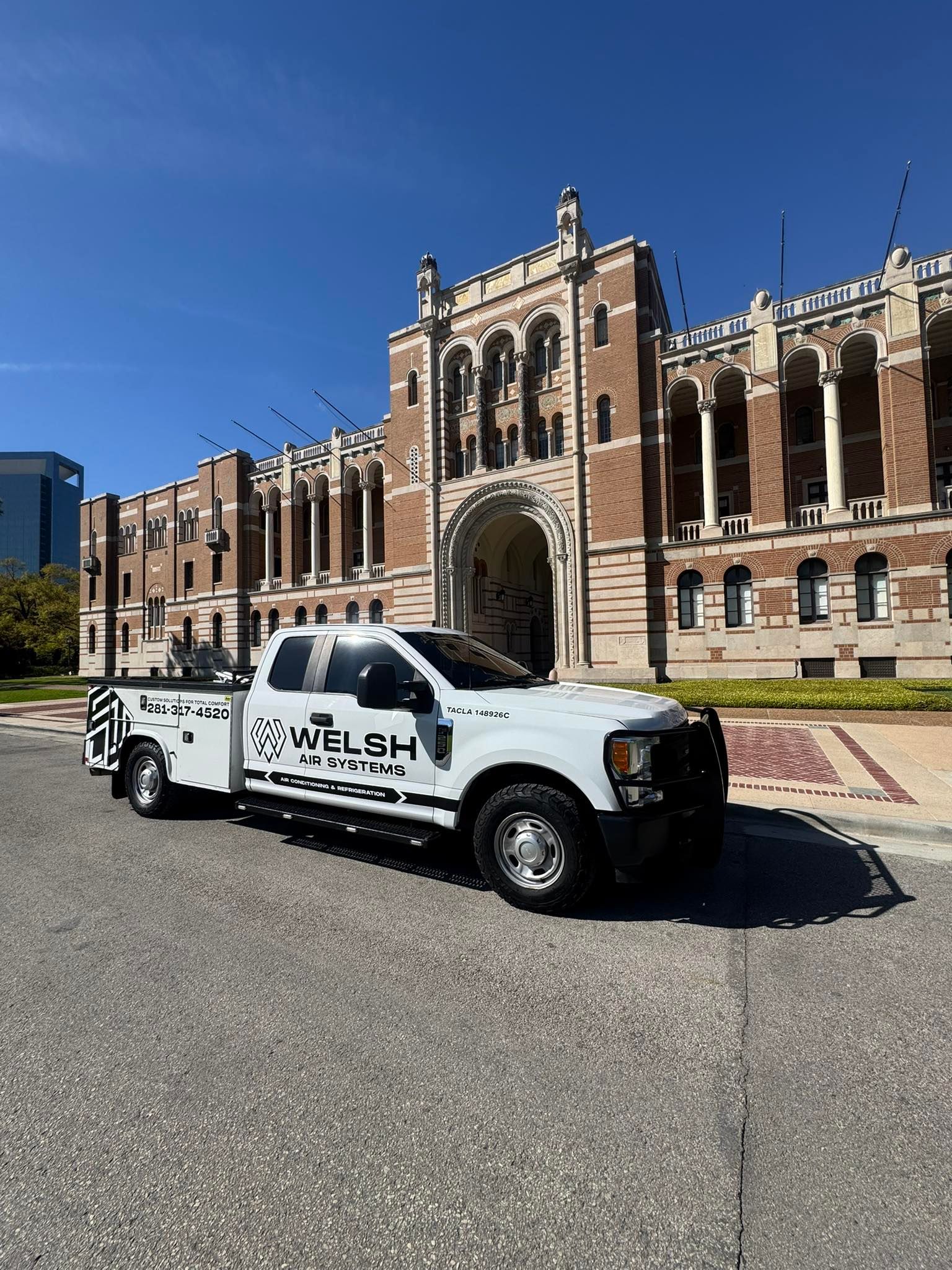 White utility truck parked before a historic brick building under a clear blue sky.