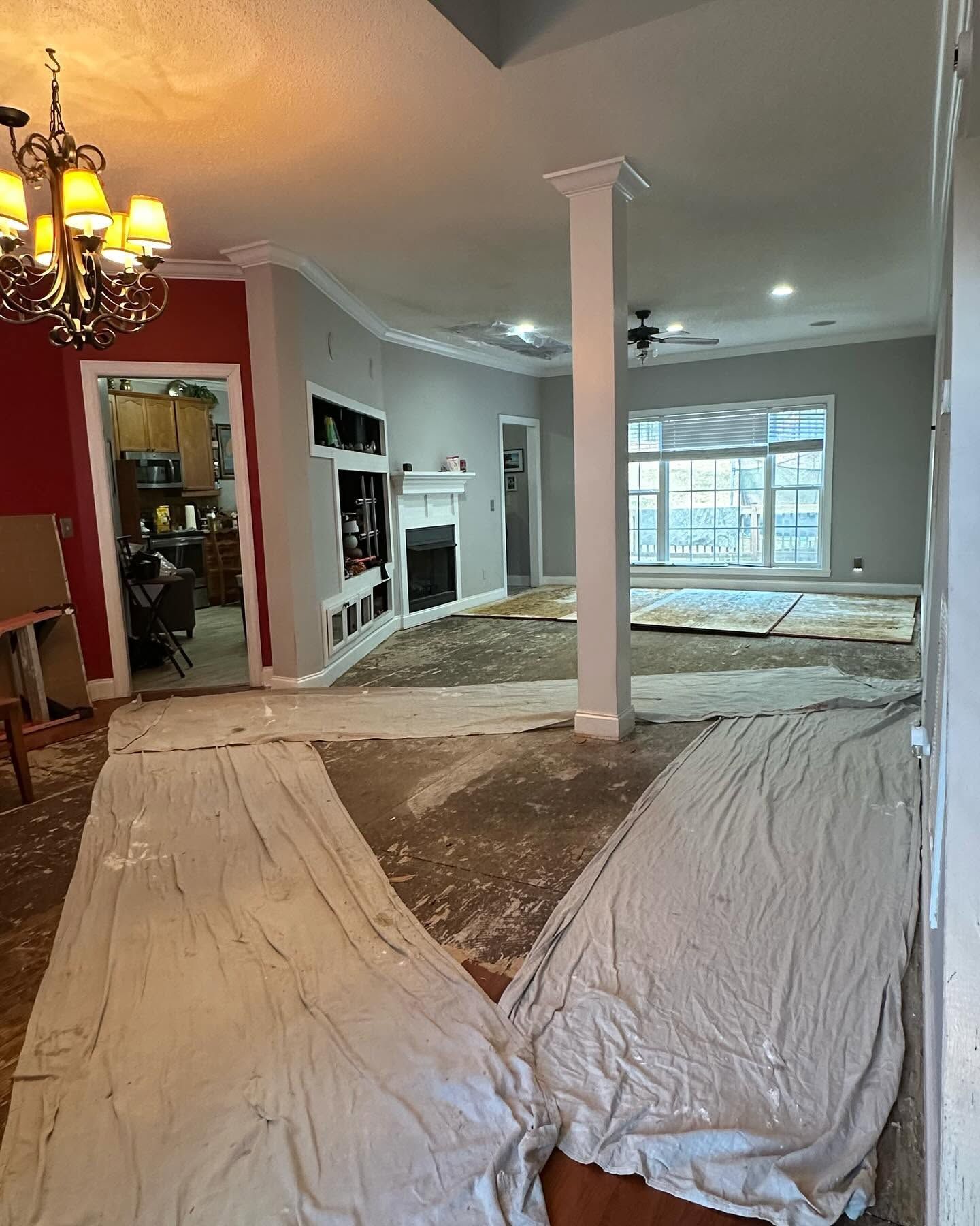 Living room under renovation with plastic-covered floors, exposed walls, and a white support column