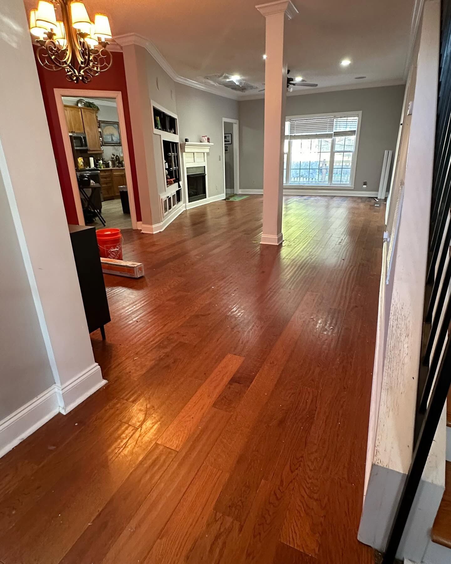 Bright empty hallway with hardwood floors, white columns, and a view into a sunlit living room