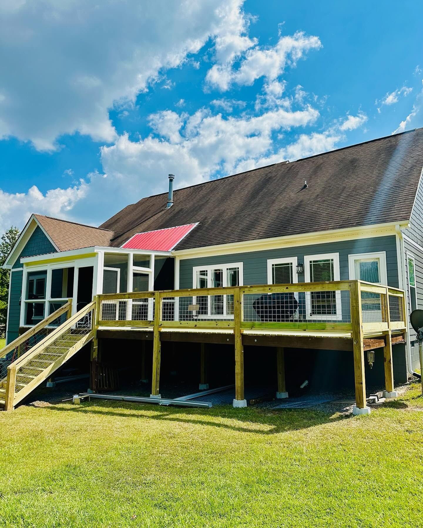 Yellow house with a large wooden deck and stairs under a blue sky