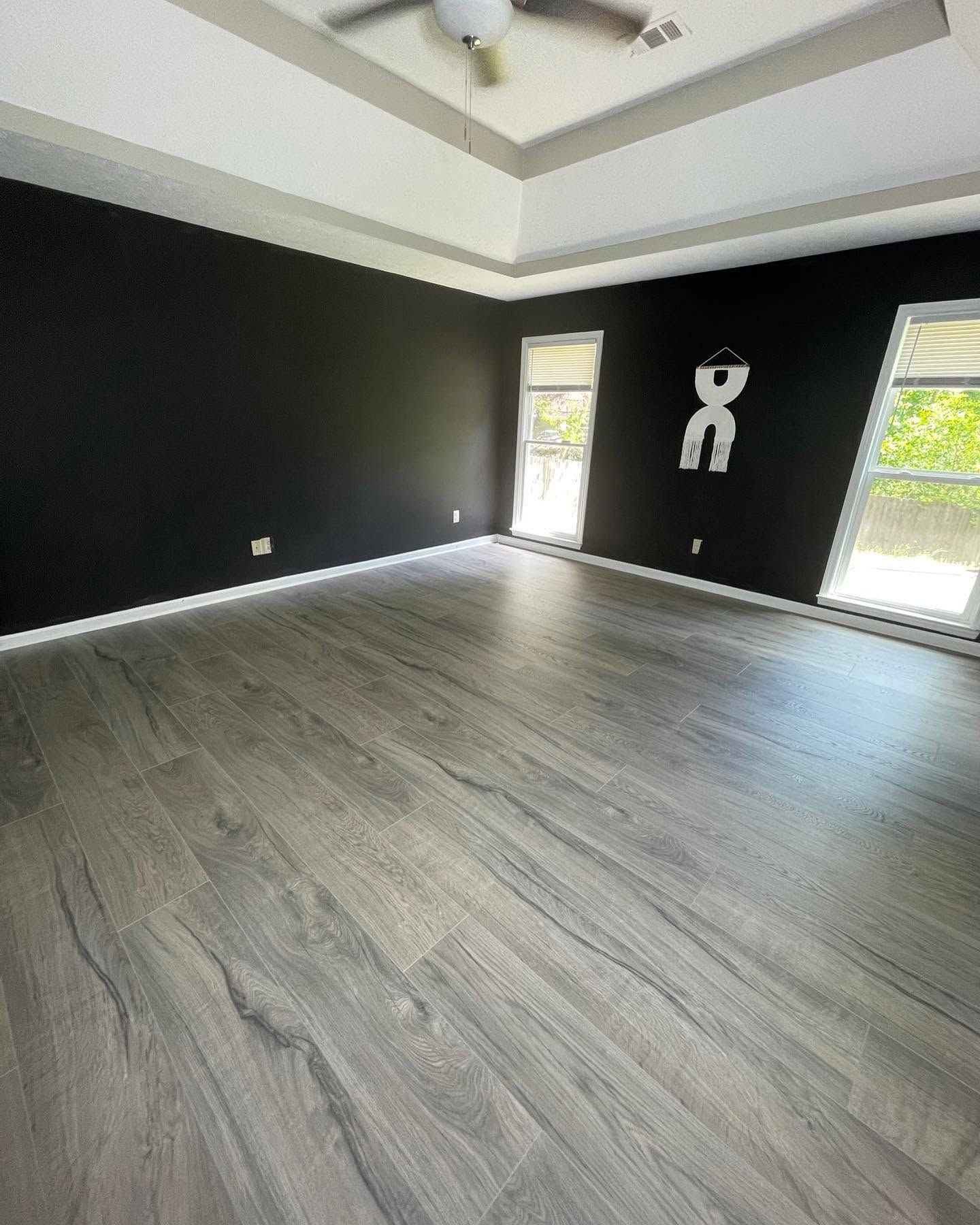 Empty modern room with gray wood floors, black walls, and two tall windows